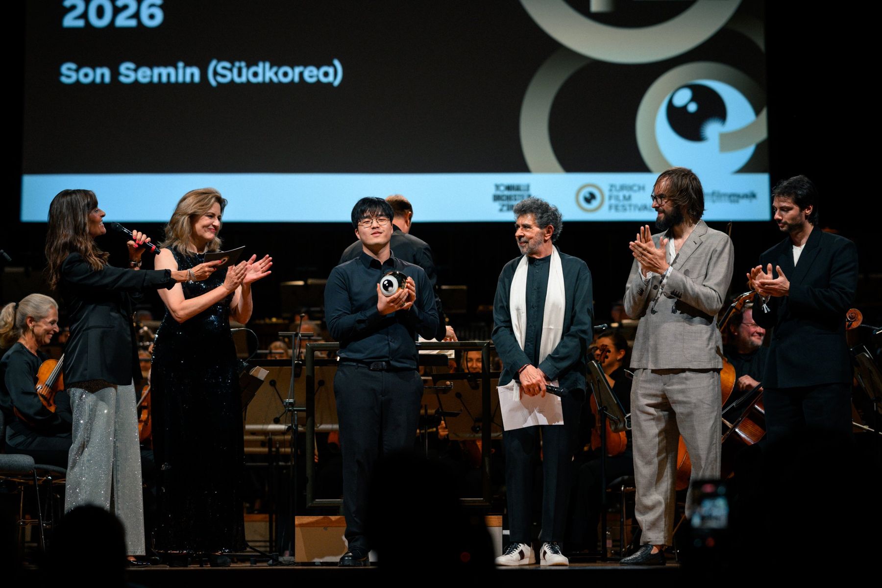 Semin Son holding the Golden Eye on stage at the Tonhalle, applauded by the jury